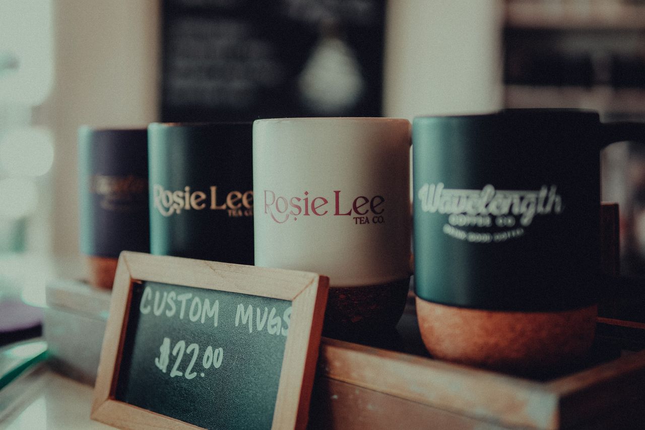 Crafting Captivating Headlines: Your awesome post title goes here Close-up of custom coffee mugs in a cafe with a price sign, highlighting product details.